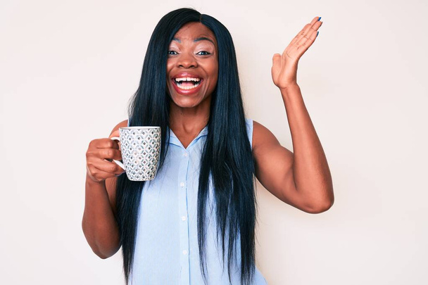 Nuori afrikkalainen amerikkalainen nainen kahvilla juhlii voittoa hymyillen ja voittajan ilme kohotetuin käsin  - Valokuva, kuva