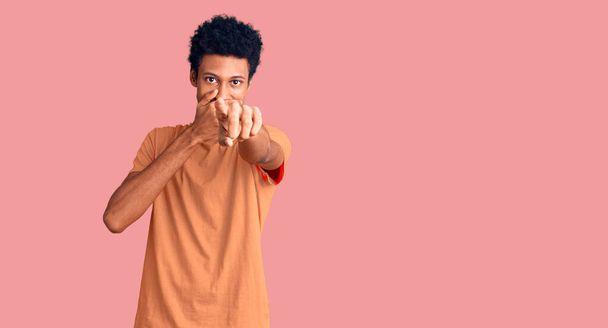 Jonge Afro-Amerikaanse man met casual kleding die je uitlacht, wijzend met de vinger naar de camera met hand over mond, schaamte uitdrukking  - Foto, afbeelding