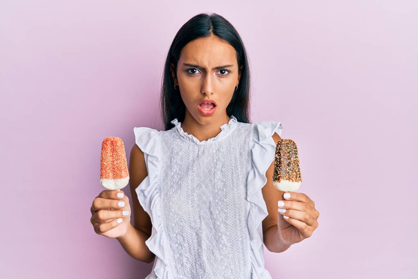 Jeune femme arabe brune tenant de la crème glacée dans le visage choqué, à l'air sceptique et sarcastique, surprise avec la bouche ouverte  - Photo, image