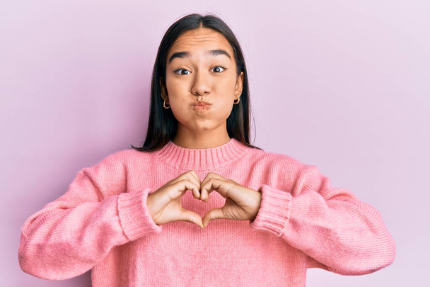 Young asian woman doing heart symbol with hands puffing cheeks with funny face. mouth inflated with air, catching air.  - Φωτογραφία, εικόνα