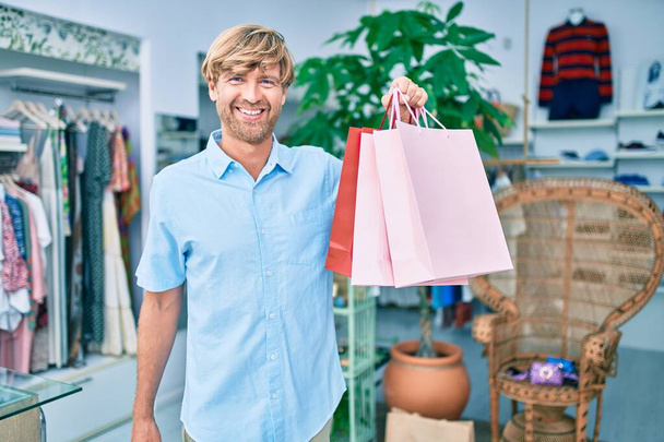 Hezký kavkazský muž usmívá šťastný nakupování v maloobchodě v nákupním centru - Fotografie, Obrázek