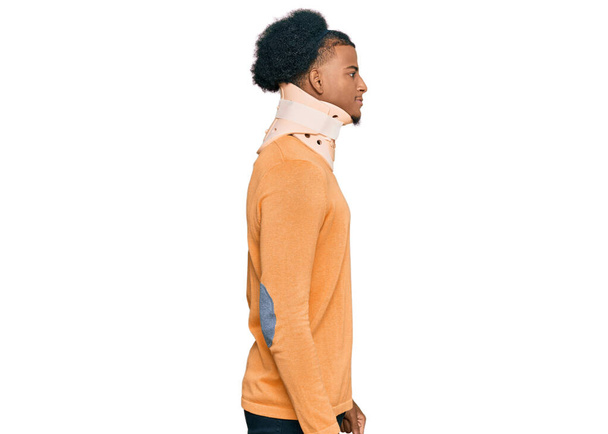 Afrikanisch-amerikanischer Mann mit Afro-Haaren trägt Halswirbelkragen zur Seite schauen, entspannen Profil Pose mit natürlichem Gesicht mit selbstbewusstem Lächeln.  - Foto, Bild