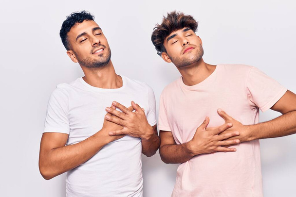 Young gay couple wearing casual clothes smiling with hands on chest with closed eyes and grateful gesture on face. health concept.  - Photo, Image