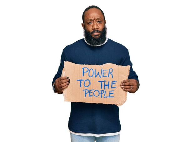 Mladý africký Američan drží moc k lidem banner myšlení postoj a střízlivý výraz hledá sebevědomí  - Fotografie, Obrázek