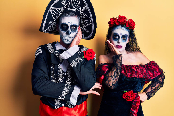 Mladý pár nosí mexický den mrtvých kostým přes žluté myšlení vypadá unaveně a znuděný deprese problémy se zkříženými pažemi.  - Fotografie, Obrázek