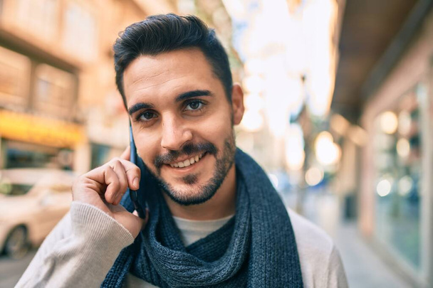 Giovane uomo ispanico sorridente felice utilizzando smartphone in città. - Foto, immagini
