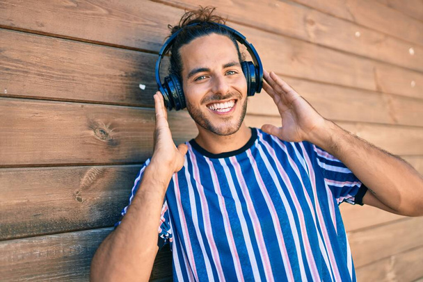 若いヒスパニック系の男は、市内でヘッドフォンを使用して音楽を聞いて幸せな笑顔. - 写真・画像