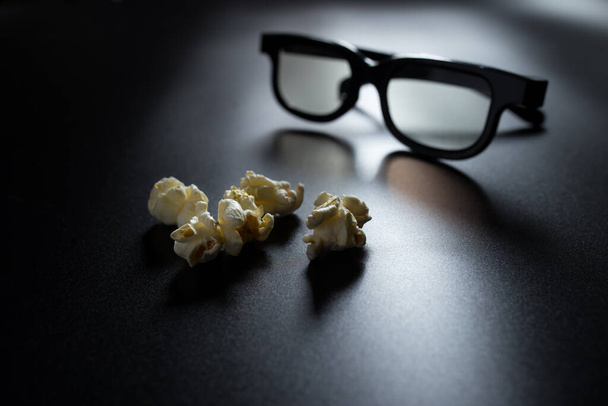 Fzlakes von Popcorn Nahaufnahme auf schwarz mit 3D-Brille bläulich auf Hintergrund. - Foto, Bild