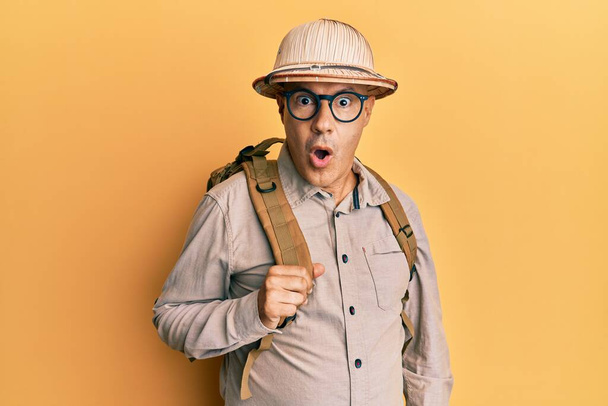 Middle age bald man wearing explorer hat and backpack scared and amazed with open mouth for surprise, disbelief face  - Photo, image