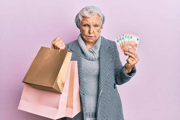 シニア白髪の女性のショッピングバッグやユーロ紙幣懐疑的かつ神経を保持し、問題のために動揺を眉をひそめて。否定的な人.  - 写真・画像