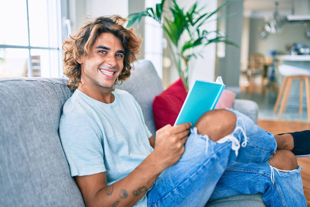 Jeune homme hispanique souriant livre de lecture heureux à la maison - Photo, image