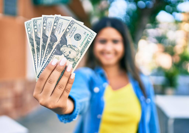 Young latin woman smiling happy holding usa dollars banknotes at city. - Zdjęcie, obraz