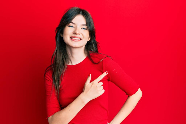 Молодая красивая кавказская девушка в непринужденной красной рубашке, весело улыбающаяся, указывая рукой и пальцем в сторону.  - Фото, изображение