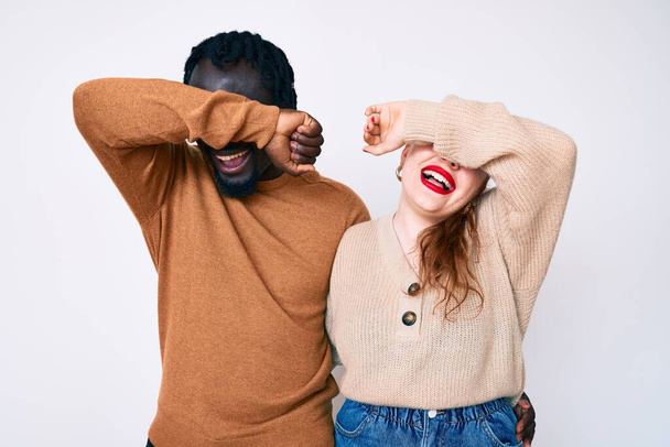 Interracial Paar in lässiger Kleidung lächelnd fröhlich spielend gucken ein Buh mit Händen Gesicht zeigen. überrascht und aufgeregt  - Foto, Bild