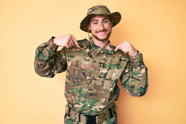 Young caucasian man wearing camouflage army uniform looking confident with smile on face, pointing oneself with fingers proud and happy.  - Φωτογραφία, εικόνα
