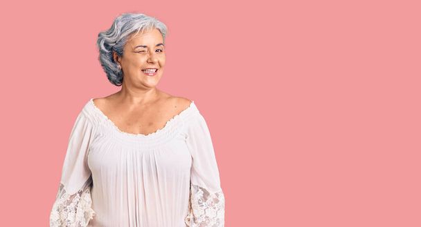 Mujer mayor con el pelo gris con el estilo bohemio guiño mirando a la cámara con expresión sexy, cara alegre y feliz.  - Foto, imagen