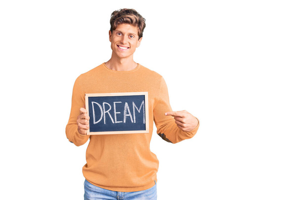 Young handsome man holding blackboard with dream word smiling happy pointing with hand and finger  - Fotografie, Obrázek