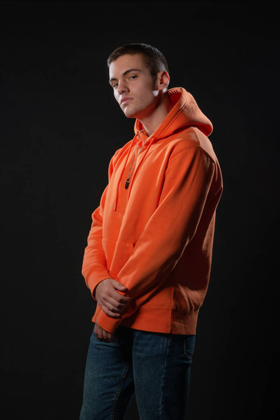 Közelkép portré egy jóképű férfi modell néz komoly, miközben pózol narancssárga kapucnis belül stúdió - Fotó, kép