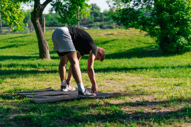 Sporty young man practicing crow pose or bakasana, yoga asana, outdoors in a park - Photo, Image