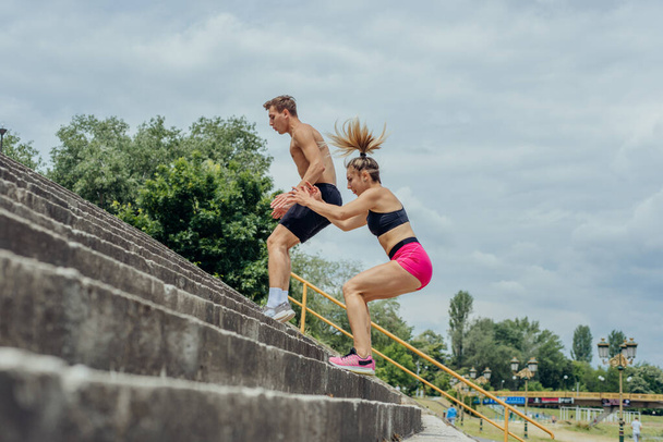 Imagen vista lateral de una pareja deportiva activa saltando por las escaleras en un parque - Foto, Imagen
