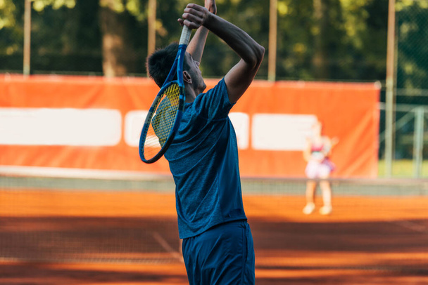 Zadní pohled na tenistu připraveného sloužit na hliněném hřišti v modrém sportovním oblečení - Fotografie, Obrázek