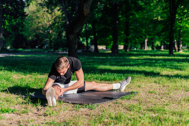 Healthy young man doing outdoors warmup stretching exercises on a fitness mat - Photo, Image
