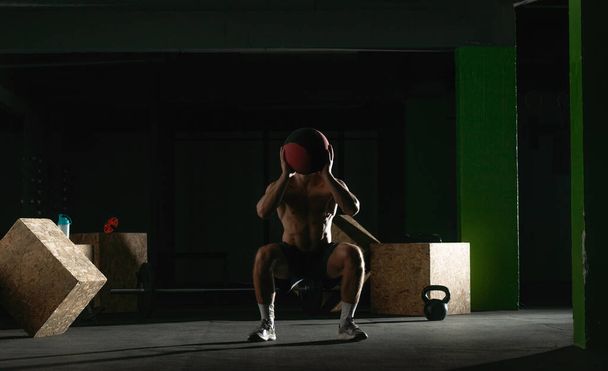 Fit άνθρωπος ρίχνουν ιατρική μπάλα κάνει μπάλα slam ενάντια στο πάτωμα του γυμναστηρίου ή ώμου πατήστε άσκηση. - Φωτογραφία, εικόνα