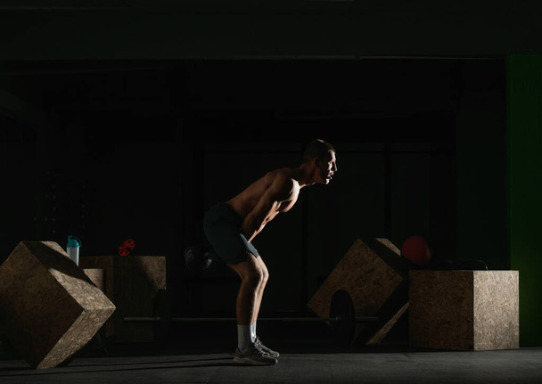 High contrast side view photo of a healthy fitness guy doing workout using a kettlebell - Foto, afbeelding