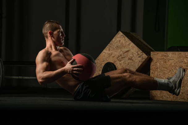 Tişörtsüz profesyonel atlet, Rus karın kası egzersizi yapıyor. Kapalı alanda antrenman yapan formda bir erkek sporcunun yakın plan fotoğrafı.. - Fotoğraf, Görsel