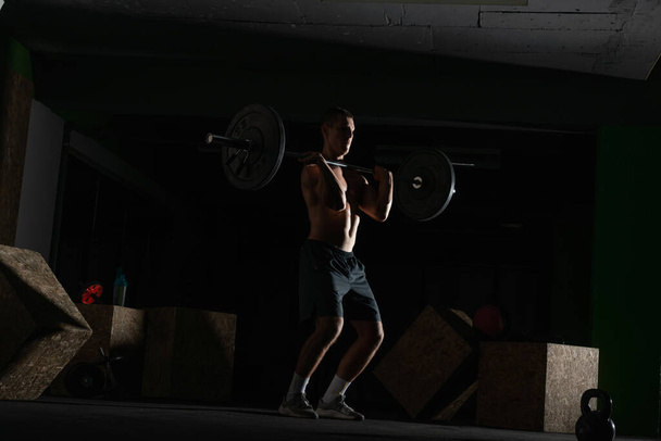 Silhouette of a fit strong shirtless athlete doing squats. Weight lifting workout concept. - Photo, Image