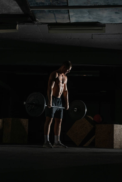 Силуэт силуэта сильного спортсмена без рубашки, делающего приседания. Концепция поднятия тяжестей. - Фото, изображение