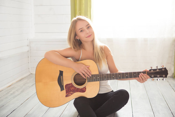 少女はギターと歌を演奏する。自宅で音楽を勉強長い髪を持つ若い女性。女性は床に座ってアコースティックギターを演奏し、自宅で一人で歌う. - 写真・画像