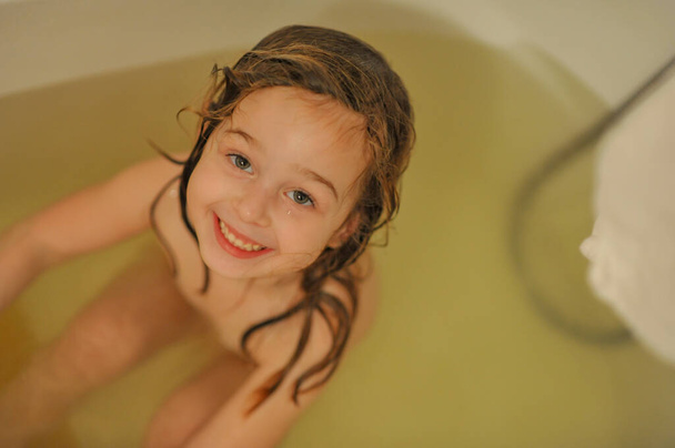 Édes kislányka fürdés közben. A kislány egy fehér fürdőkádban fürdik. Gyermekkori tisztaság fürdés - Fotó, kép