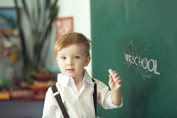 Boy with chalk over green chalkboard. Preschool or school concept. - 写真・画像