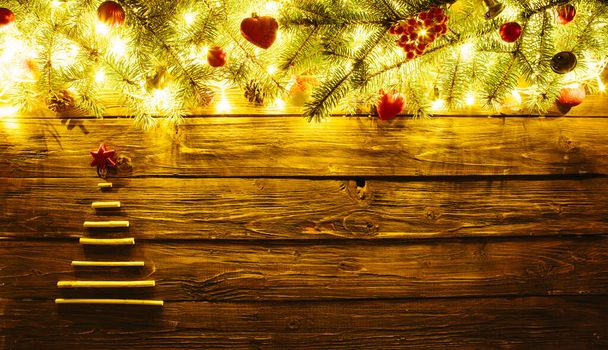 Blurred Christmas background, with fir branches, xmas tree from dry sticks, fairy lights and christmas decorations on brown wooden plank - Foto, Bild