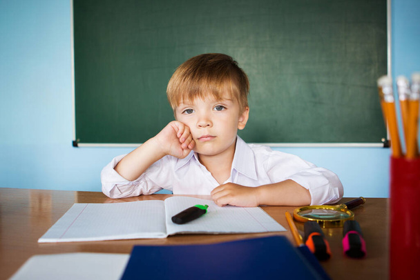 Little cute boy at school ponders a difficult school task and looks into the camera - Foto, Imagen