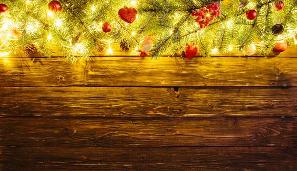 Christmas tree branch and lights on wooden background. View with copy space Blurred Christmas background, with fir branches, fairy lights and christmas decorations on brown wooden plank - Фото, изображение