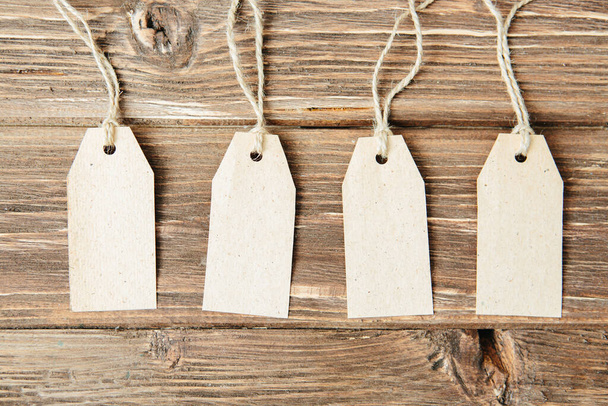 set of four tags hanging on rope on wooden background Four paper blank tags with rope on wooden background. - 写真・画像
