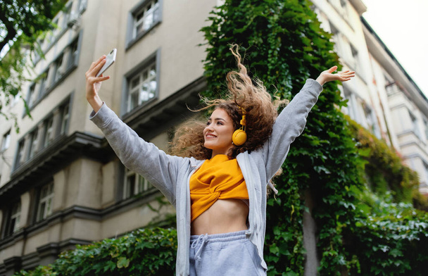 Young woman with smartphone dancing outdoors on street, tik tok concept. - Фото, зображення