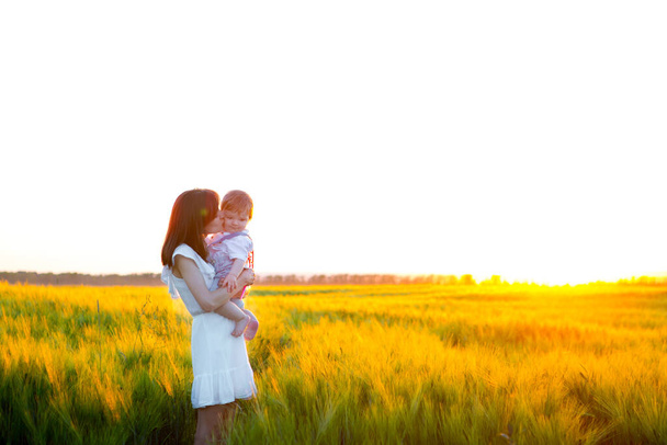Baby and mother on nature in the park. Happy mother holding baby smiling on a wheat field in sunlight. Family happiness concept. - Foto, afbeelding