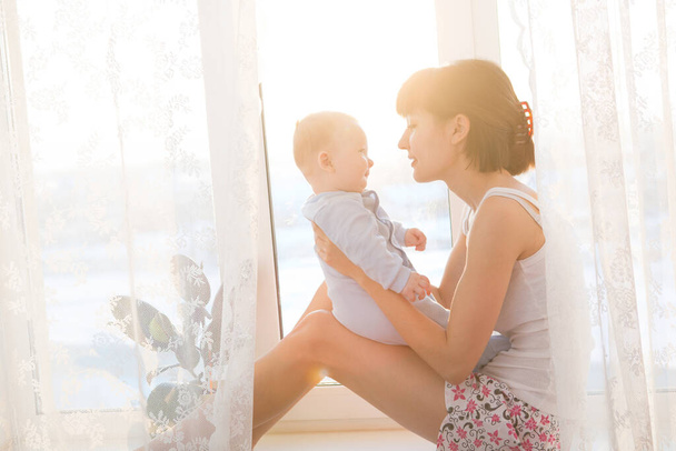 Young mother with a baby in a beautiful bedroom. Happy  mother holding adorable child baby with sunrise background - Foto, Bild