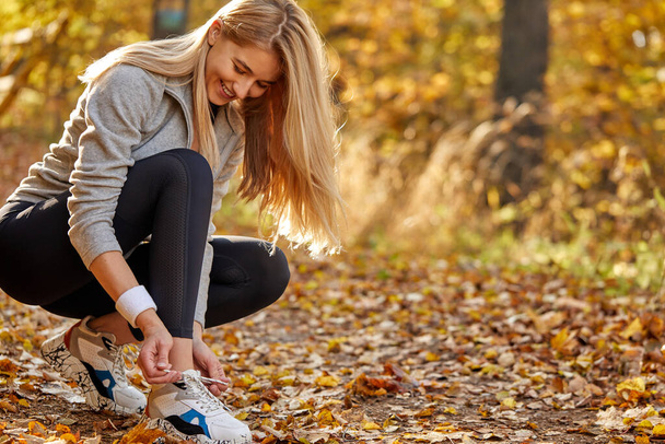caucasian young woman tie the laces on the sneakers before running outdoors - Foto, Bild