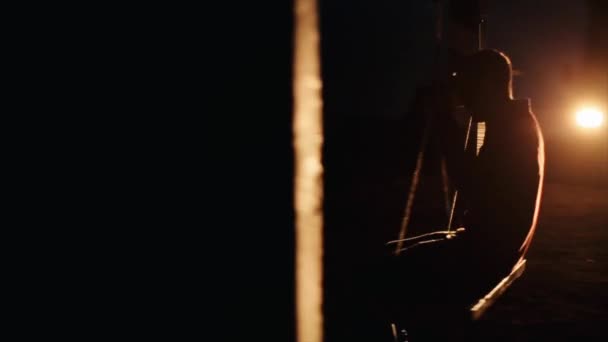 Een jongeman rijdt op een touwschommel tegen de achtergrond van fel geschakelde koplampen van een busje dat in het donker staat. Langzame beweging - Video