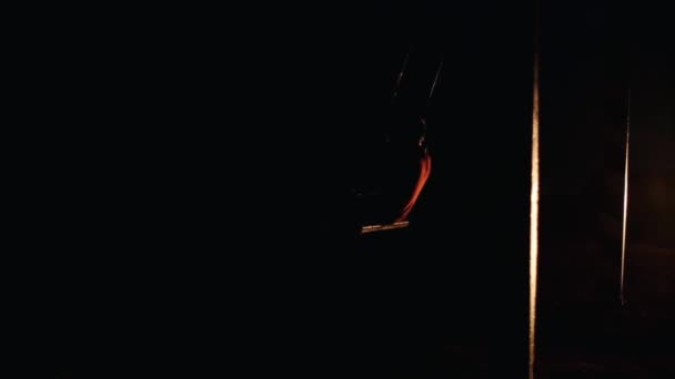 Silhouet van een jongeman die 's nachts op een touwschommel tegen de achtergrond van de koplampen van de auto zwaait. Langzame beweging - Video