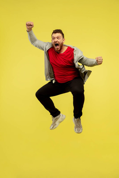 Full length portrait of young successfull high jumping man gesturing isolated on yellow studio background - Φωτογραφία, εικόνα
