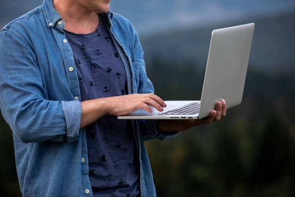 Man working outdoors with laptop in mountains. Concept of remote work or freelancer lifestyle. Cellular network broadband coverage. internet 5G. - Photo, Image