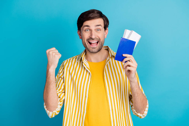 Photo of ecstatic guy win abroad travel trip lottery hold tickets raise fists wear white clothes isolated over blue color background - Photo, Image