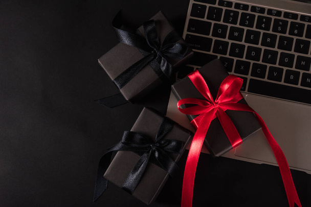 Black Friday sale online shopping commerce, Top view of gift box wrapped black paper and red bow ribbon present on a laptop computer keyboard, studio shot on black background - Foto, immagini