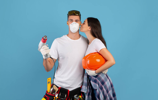 Любящая пара делает ремонт вместе, позируя со строительными инструментами на синем фоне - Фото, изображение