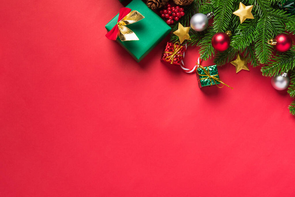 Fondo de Navidad presenta tarjeta de felicitación con vista superior sobre ramas de abeto verde y caja de regalo de decoración, temporada de celebración navideña sobre fondo de mesa rojo con espacio para copiar - Foto, Imagen